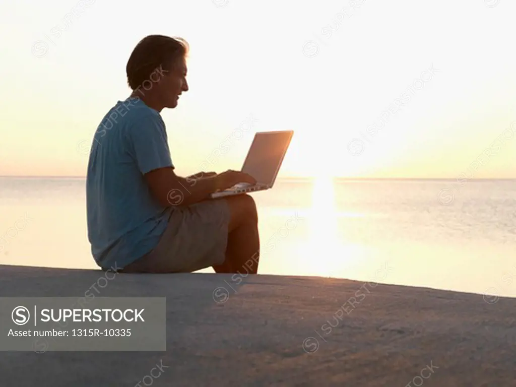 USA, Florida, Keys, Man working on laptop computer from stone walkway above sea