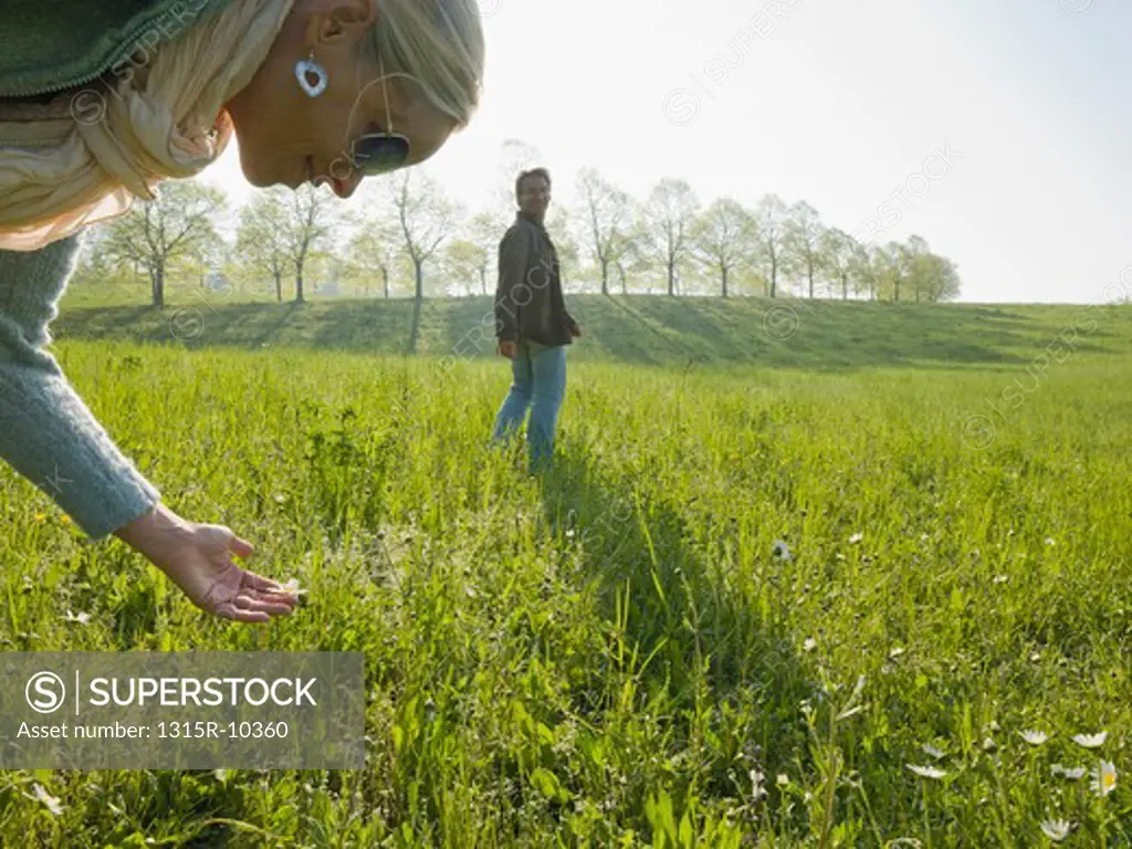 Italy, Piedmont, Woman looking at flower in meadow, man in background