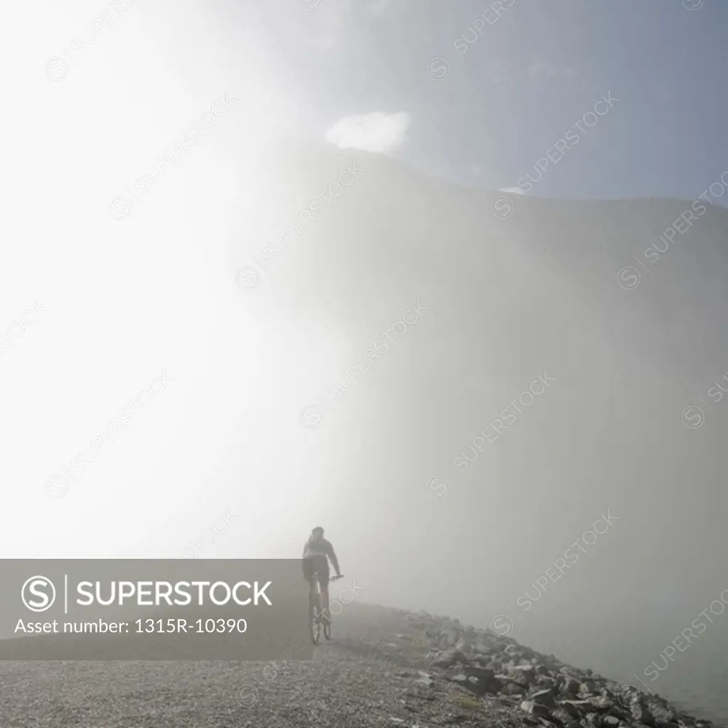 Canada, Alberta,Canmore, Silhouette of woman cycling down mountain road in fog
