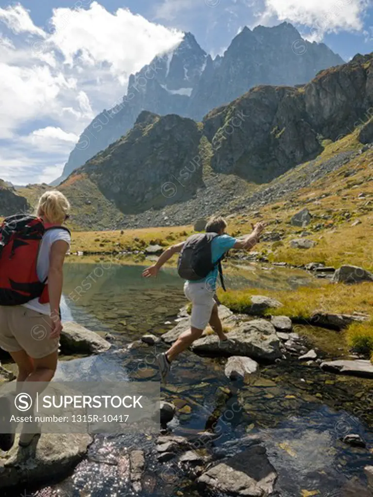 Italy, Piedmont, Couple jumping between rocks along edge of mountain lake