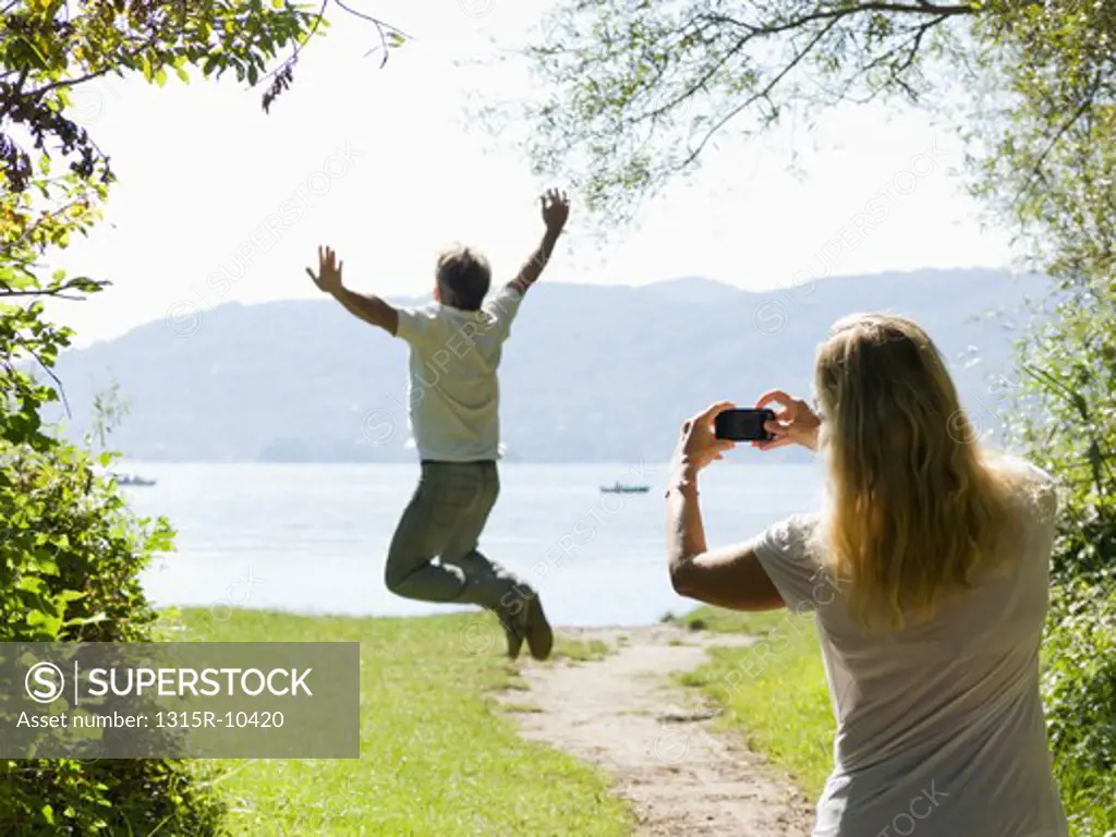 Italy, Piedmont, Lake Maggiore, Woman taking picture of man jumping for joy
