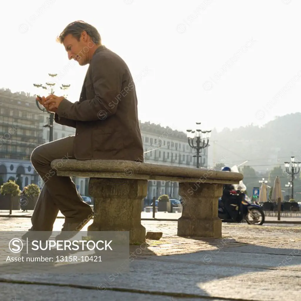 Italy, Turin, Man sending text message from bench in piazza