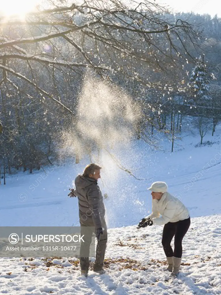 Italy, Piedmont, Couple throwing snow overhead in snowy park