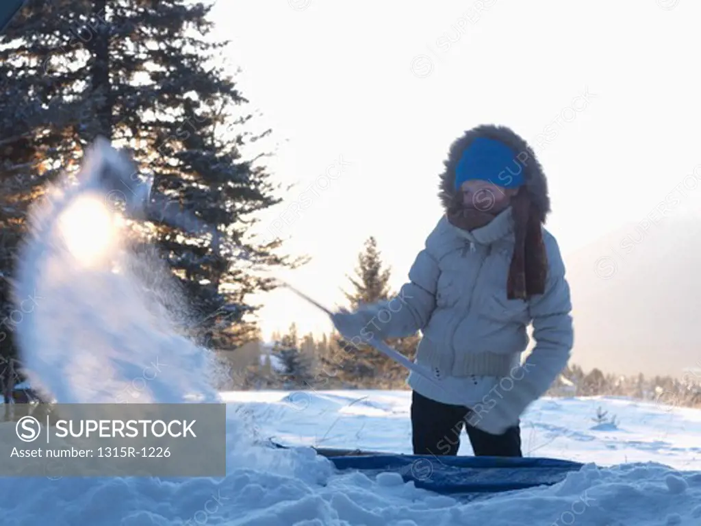 Canada, Alberta, Teenage girl brushing deep snow off trampoline, cold day