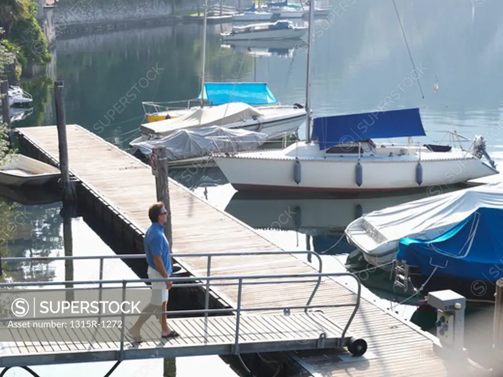 Italy, Piedmont, Lake Orta, Man walking over bridge to sailboat pier