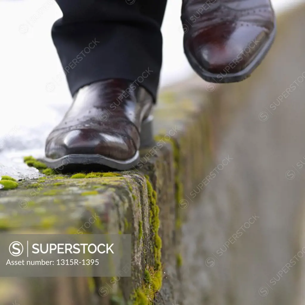 Italy, Piedmont, Turin, businessman's feet traversing icy and mossy ledge