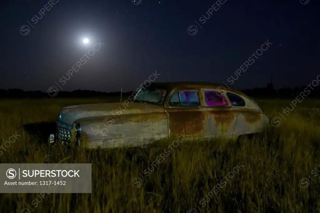 Abandoned vintage car in a field at night, USA