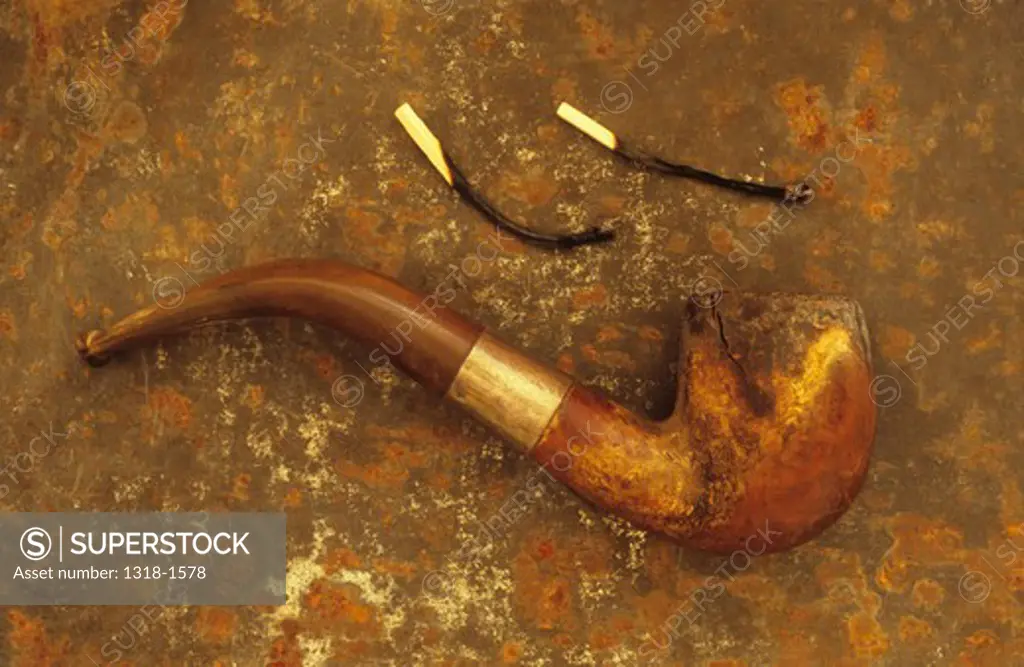 Close-up of an old smokers pipe with two burnt match sticks on a rusty metal sheet