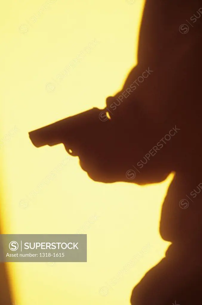 UK, Shadow in warm light of thigh and arm of figure with hand holding gun in threatening manner
