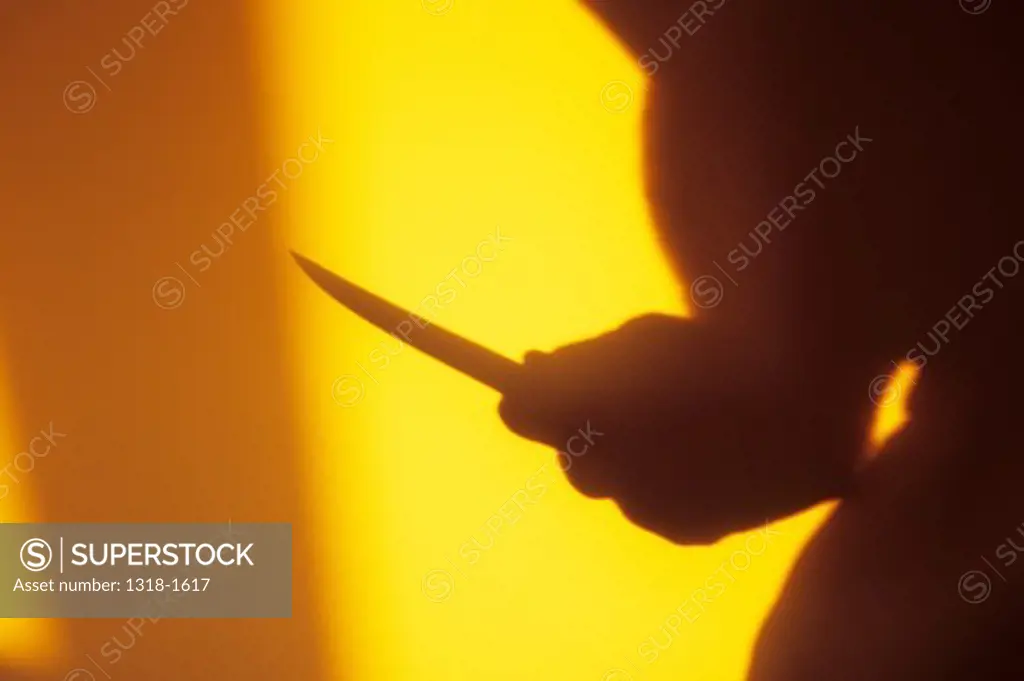 UK, Shadow in warm light of thigh and arm of figure with hand holding long-bladed knife in threatening manner