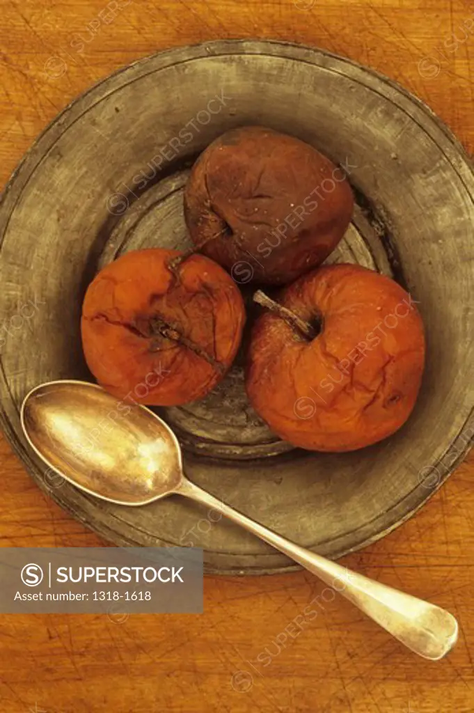 Close up of three rotten brown apples with teaspoon on tin or pewter plate on chopping board
