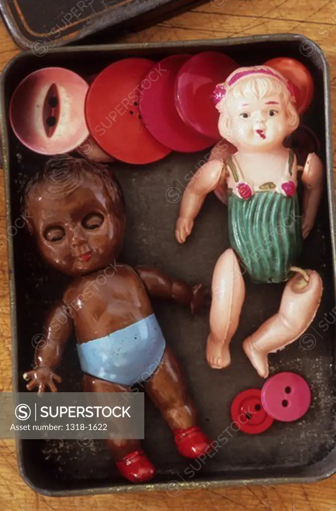 UK, Close up of tin box containing small brown skinned plastic boy doll with blue shorts white skinned celluloid girl doll with loose limbs and pink and red buttons