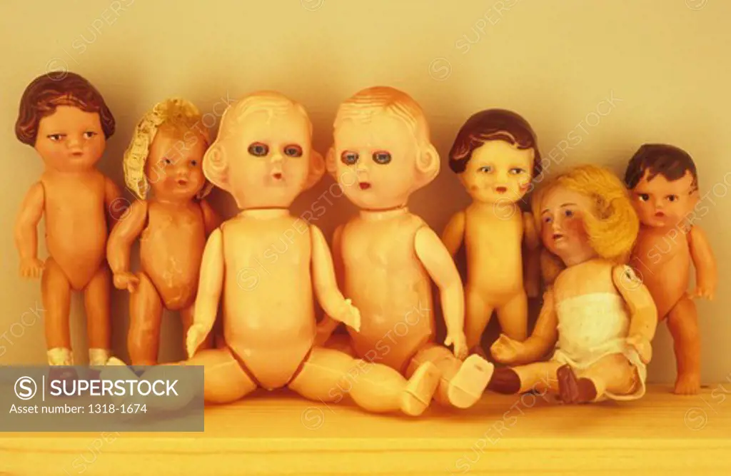 Collection of seven small early to mid-20th century traditional baby dolls lined up on wooden shelf