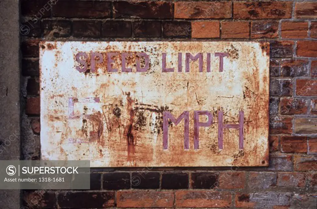 UK, England, Suffolk, Worn and rusted metal sign on weathered black and orange brick wall stating speed limit
