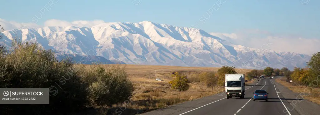 Vehicles on the road with Tian Shan Mountains in the background, Bishkek, Kyrgyzstan