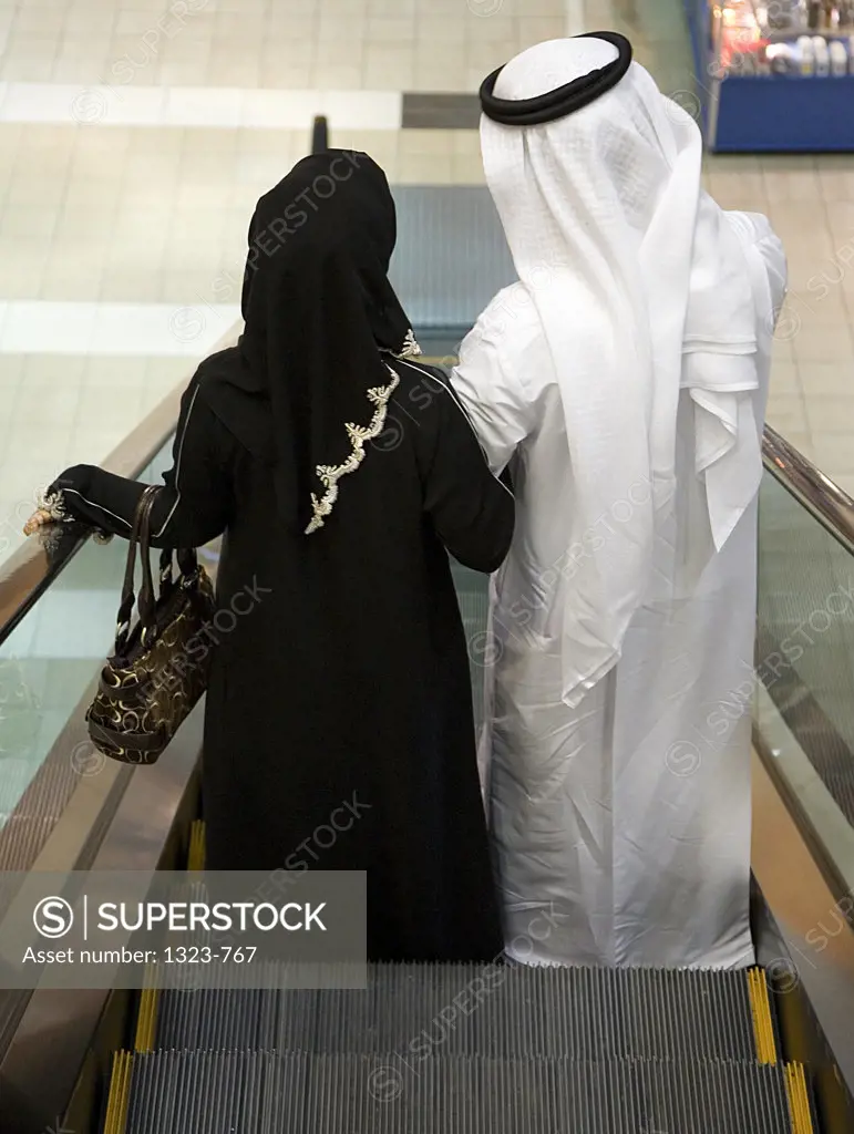 Rear view of a couple standing on an escalator in a shopping mall, Dubai, United Arab Emirates