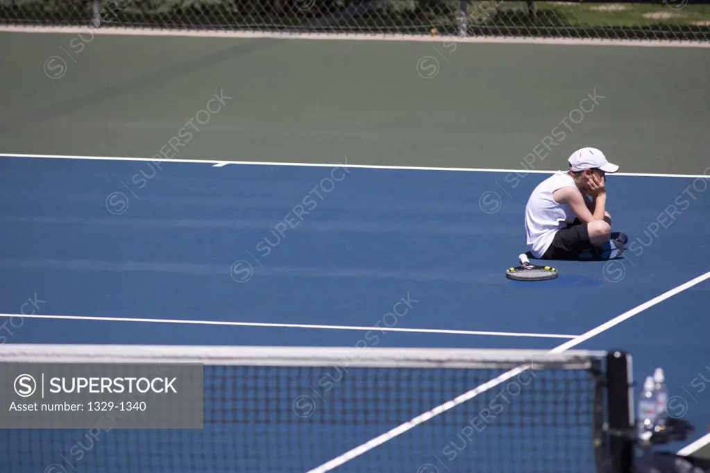 Sad boy sitting on tennis court