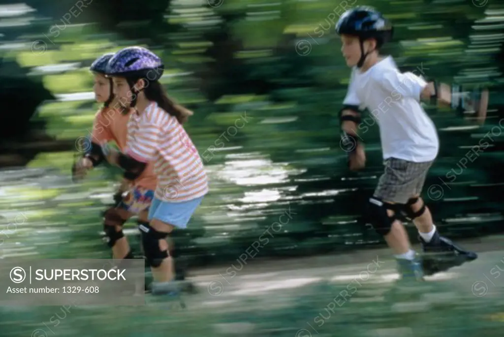 Side profile of two girls and a boy inline skating on a road