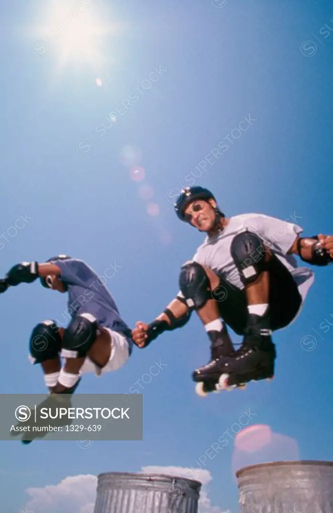 Low angle view of two young men performing stunts with inline skates