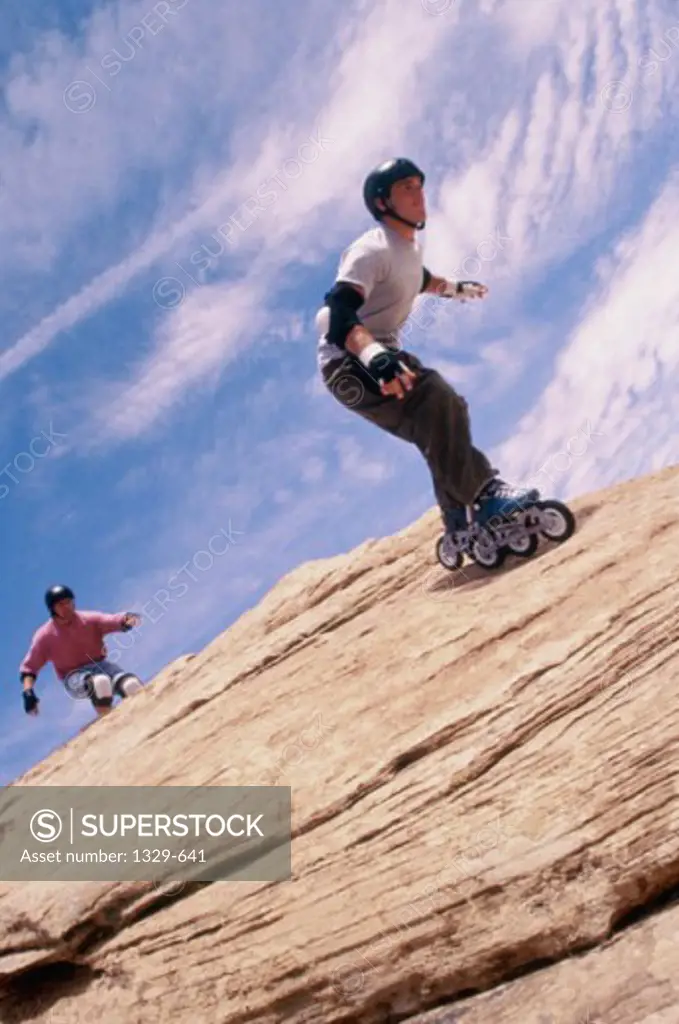 Low angle view of two young men inline skating on a rock