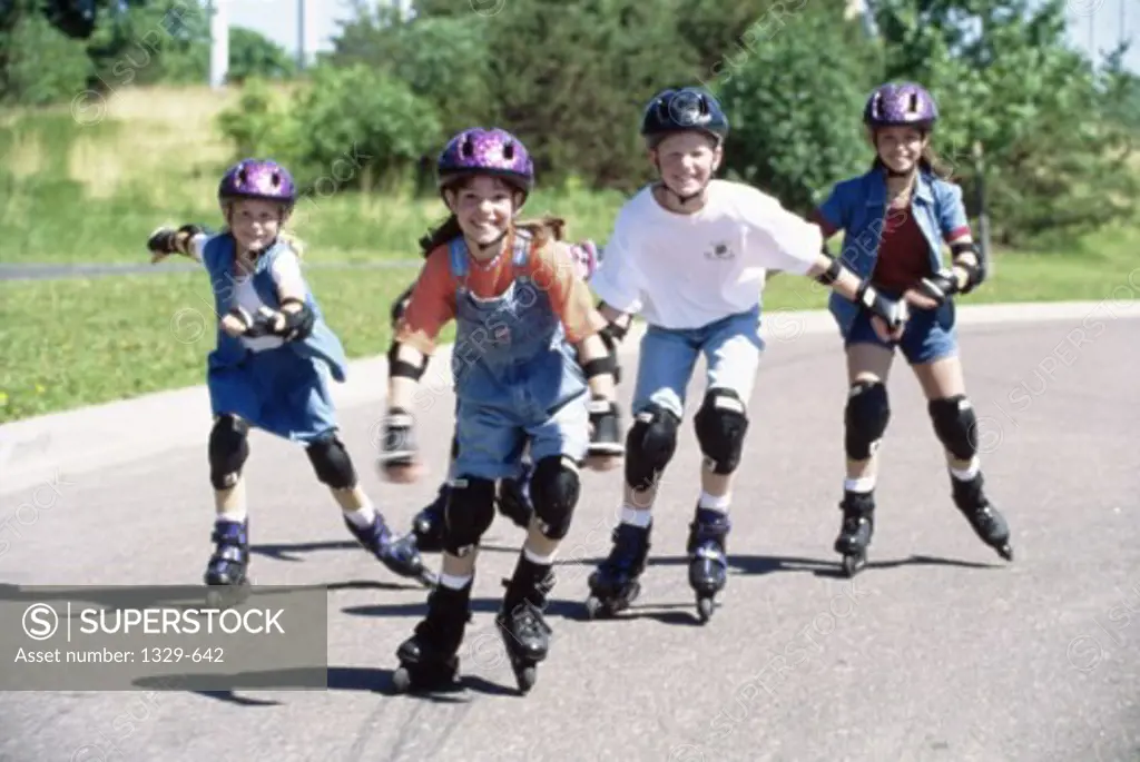 Three girls and a boy inline skating on a road