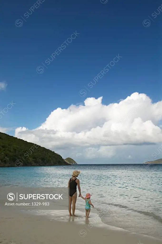 Rear view of a baby girl standing with her mother on the beach, St. Thomas, US Virgin Islands