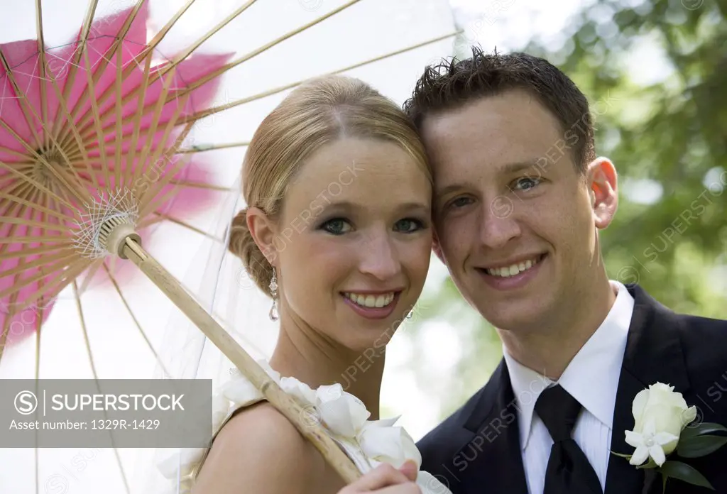 Bride and groom in their mid 20's with bride holding parasol
