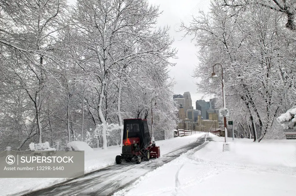 USA, Minnesota, Minneapolis, Red snow plow in white winter park looking at skyline of city