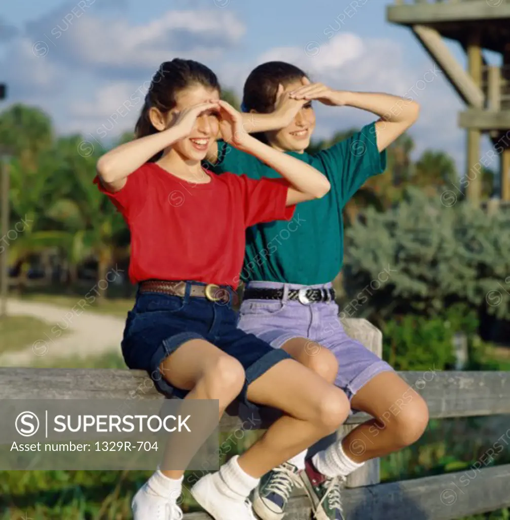 Two girls sitting on a wooden fence