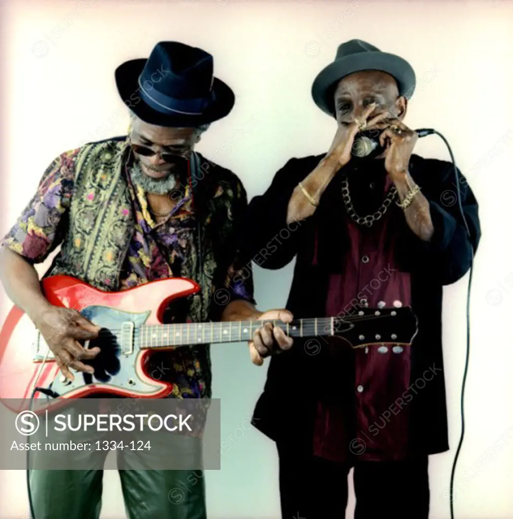 Mature man playing an electric guitar with a mature man standing beside him playing the harmonica