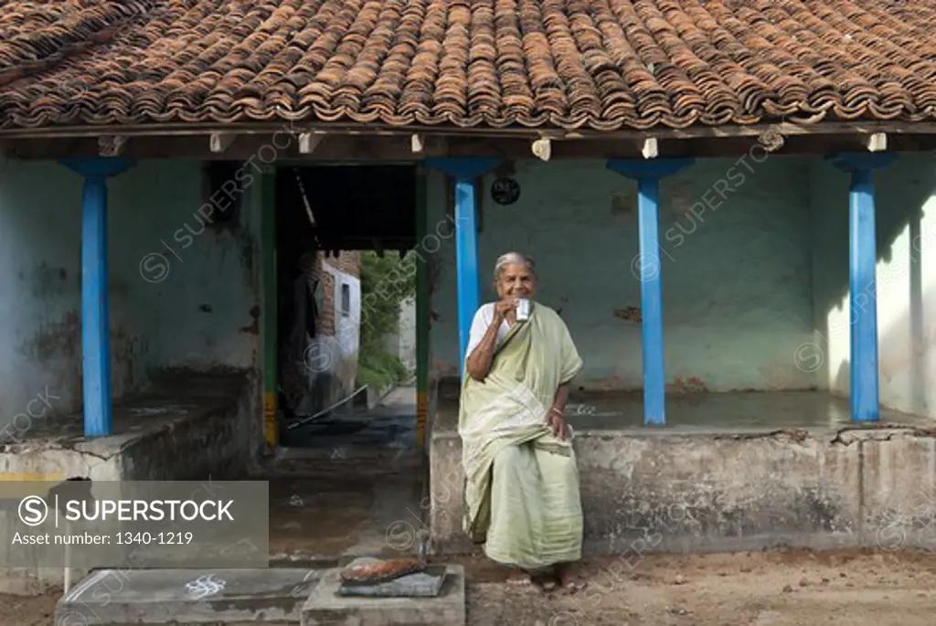 Woman sitting in front of a house and drinking tea, Kanchipuram, Tamil Nadu, India