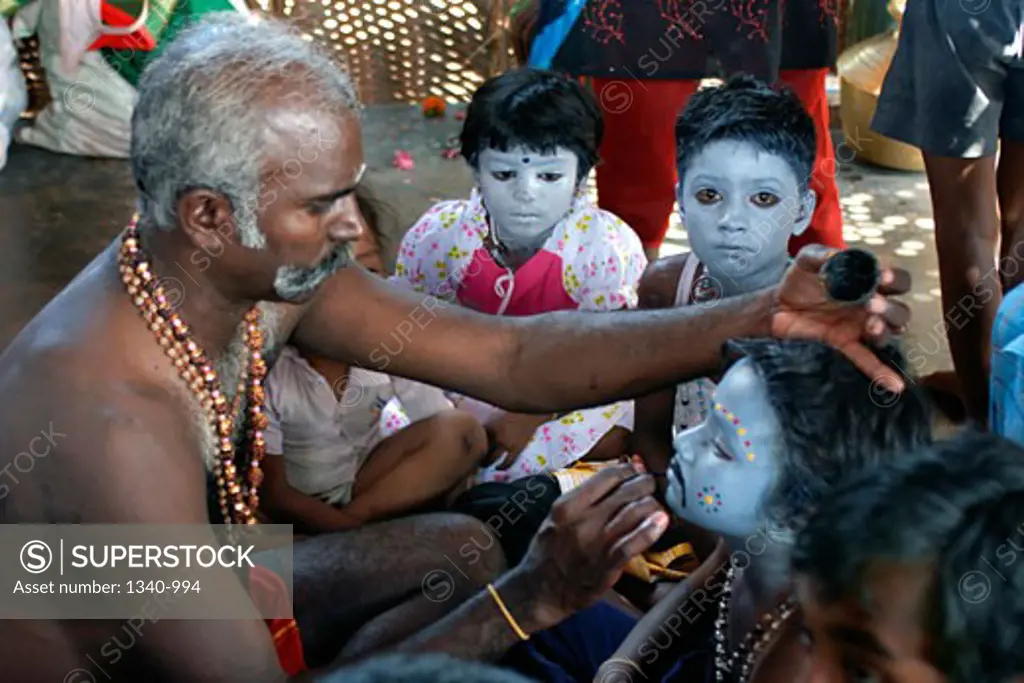 Mature man applying make-up on children for Dussehra festival, Tamil Nadu, India