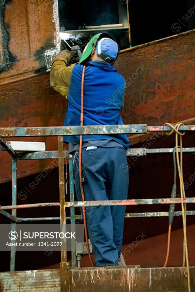 Rear view of a welder welding on a boat in a shipyard