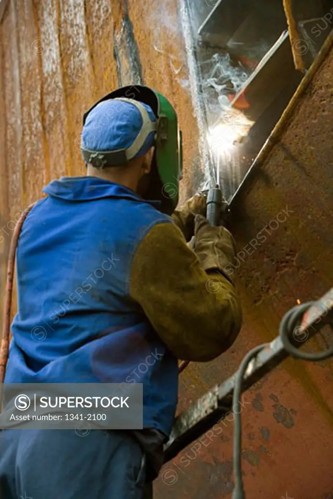 Rear view of a welder welding on a boat in a shipyard