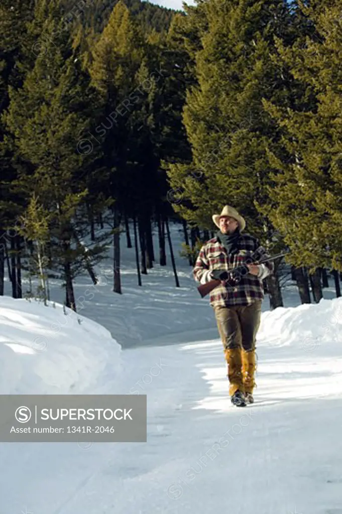 Mature man walking on snow and holding a rifle, Jackson, Wyoming, USA