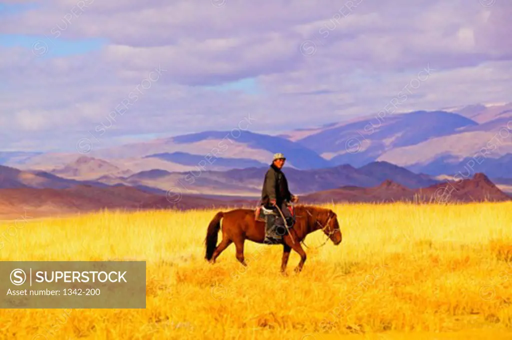 Side profile of a Kazakh man riding a horse in a field, Mongolia