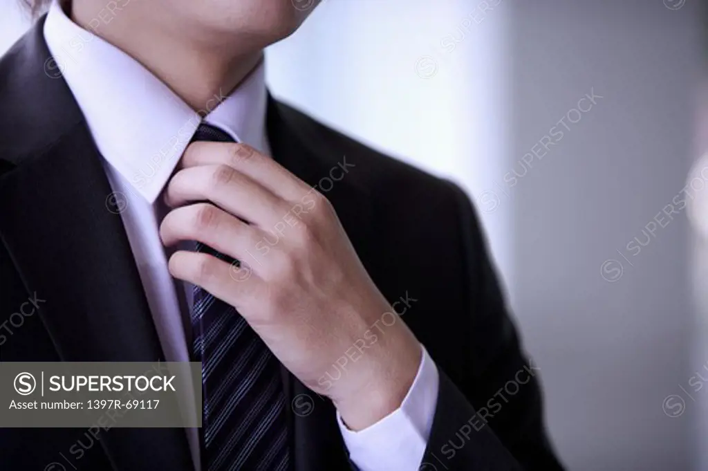 Young man holding tie with hand on chest
