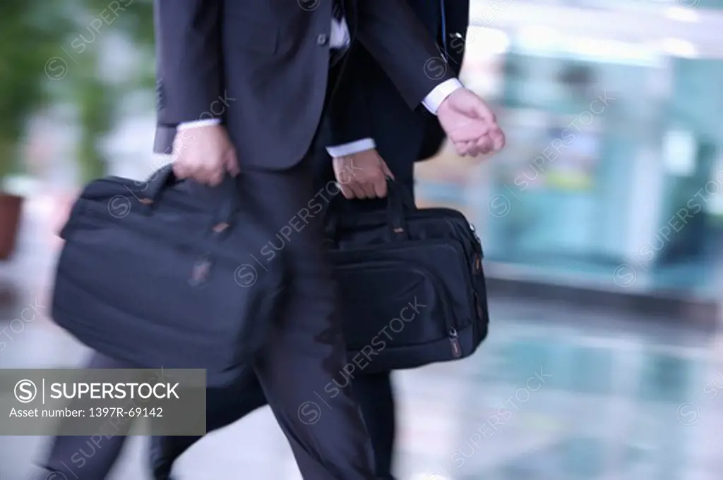 Two businessmen walking and holding briefcase together
