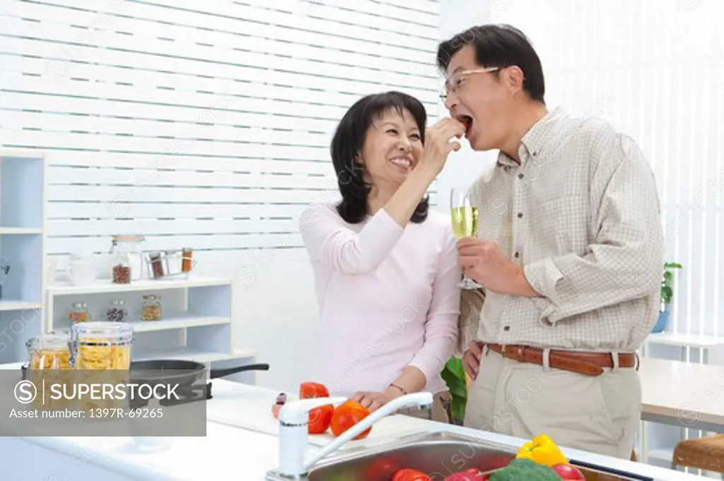Couple, Wife taking food to husband's mouth with smile in the kitchen