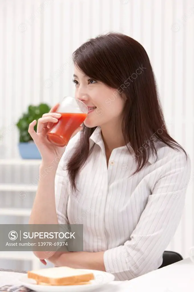 Woman drinking a glass of juice and looking away with smile
