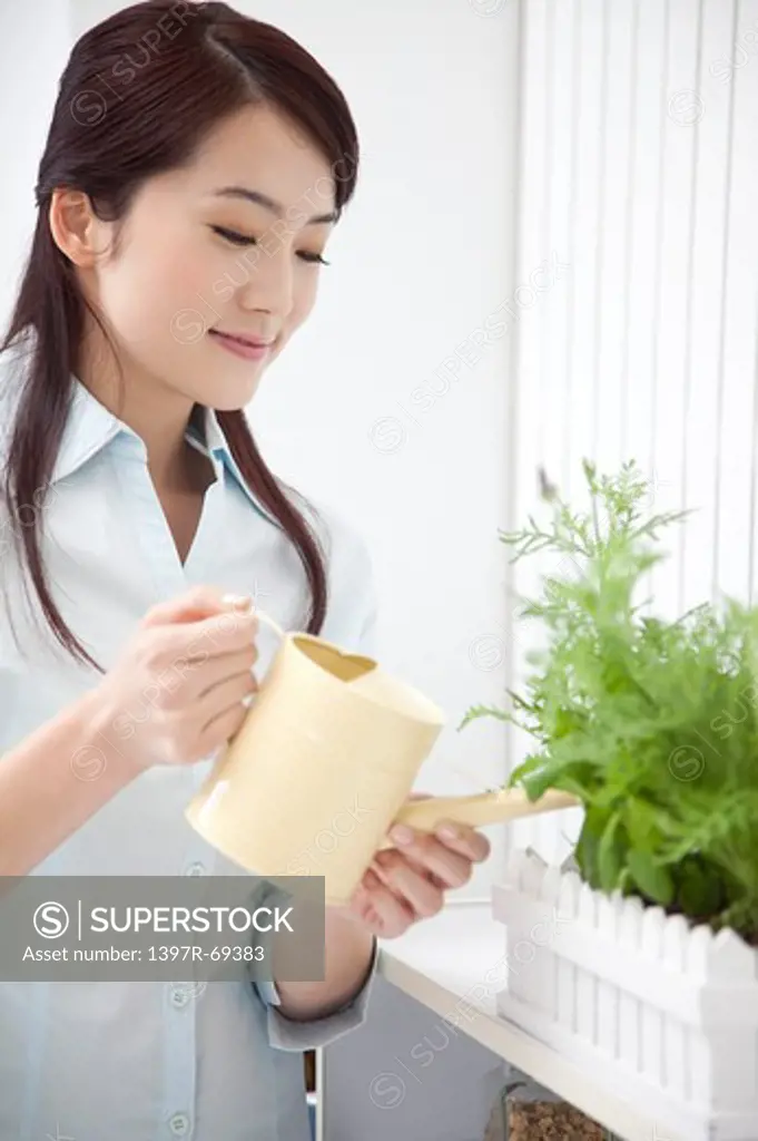 Woman holding watering can watering green plant