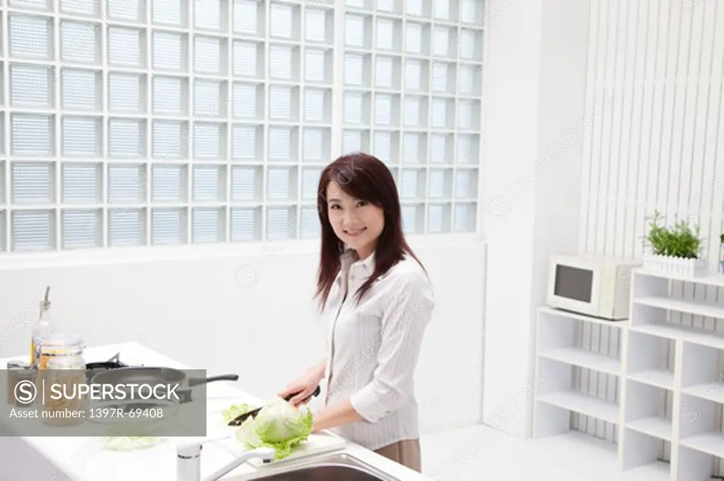 Woman chopping vegetable in the kitchen and looking at the camera with smile