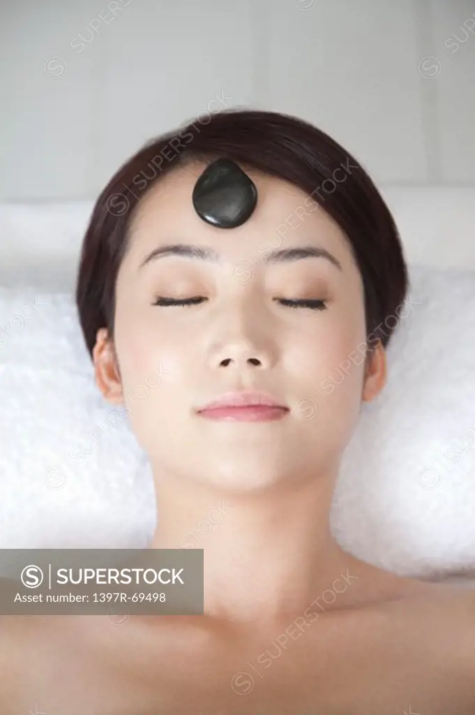 Beauty Treatment, Woman lying with eyes closed and a pebble on face