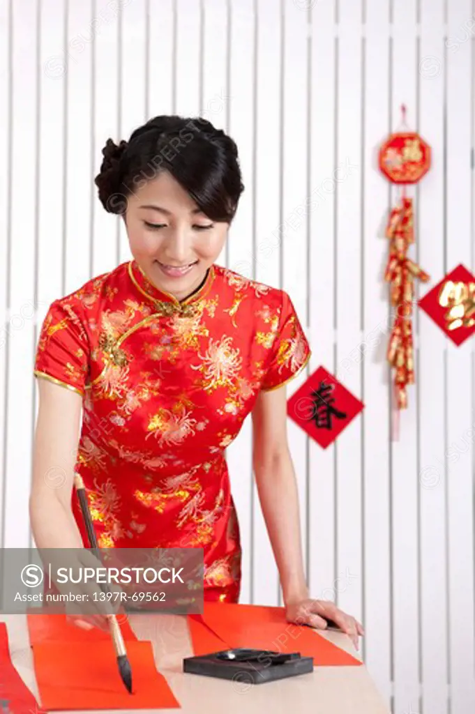 New Year, Young woman wearing Chinese traditional clothing and writing with ink brush with smile