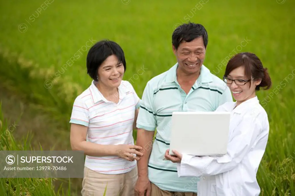 Farmer couple with expert holding laptop in rice field