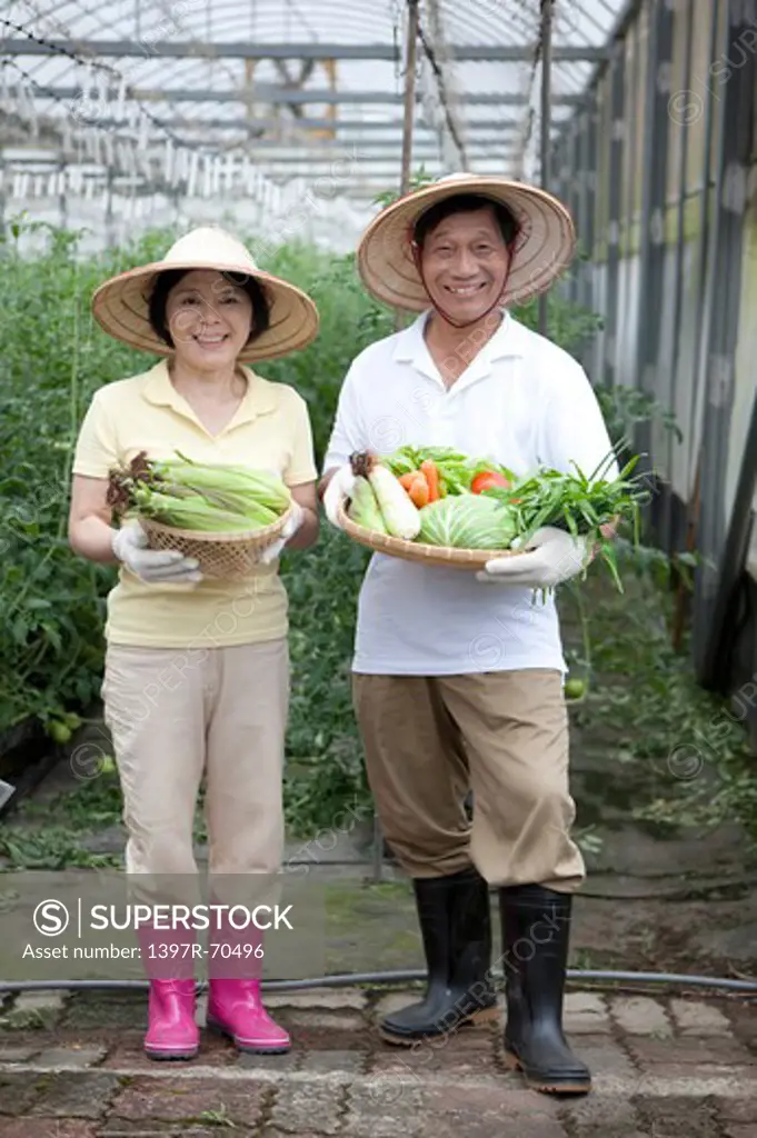 Farmer couple holding vegetables in greenhouse, smiling