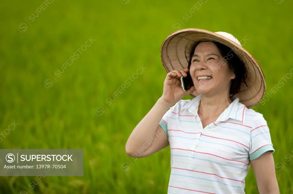 Mature farmer talking happily on mobile phone in field