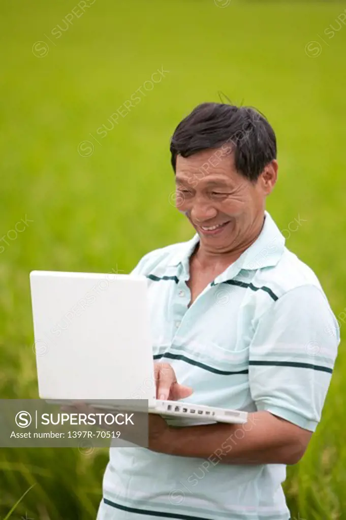 Elderly farmer using laptop in field, smiling