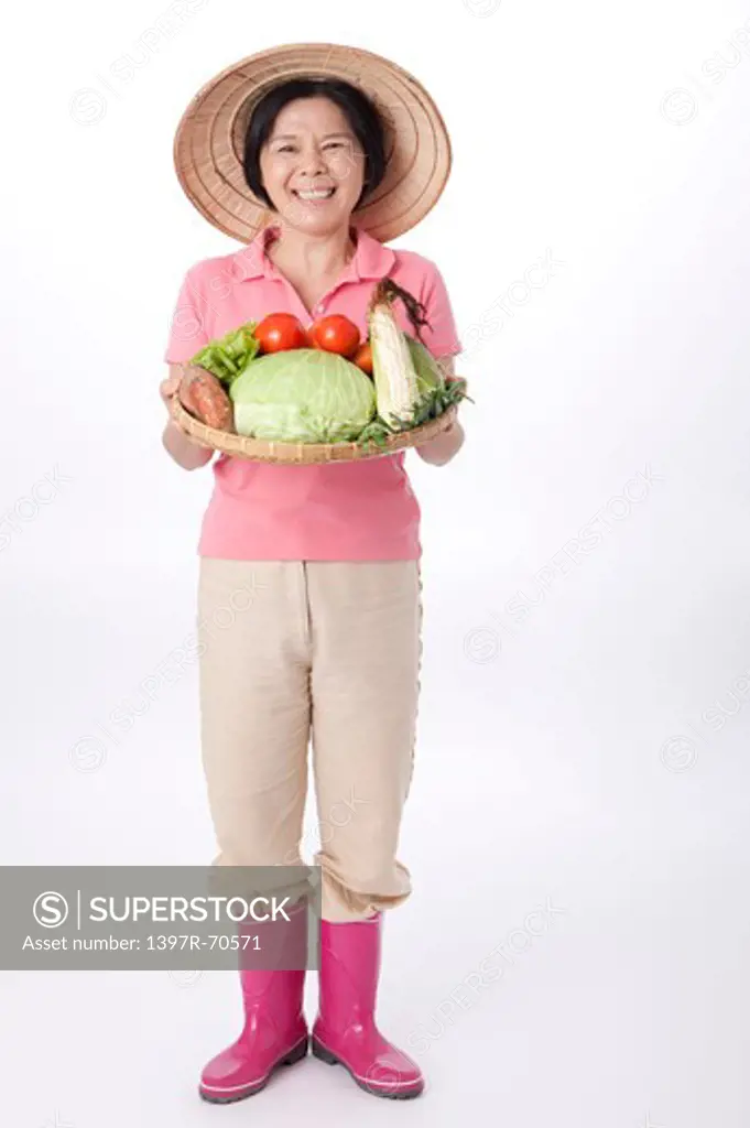 Mature farmer standing and holding a sieve of vegetables, smiling