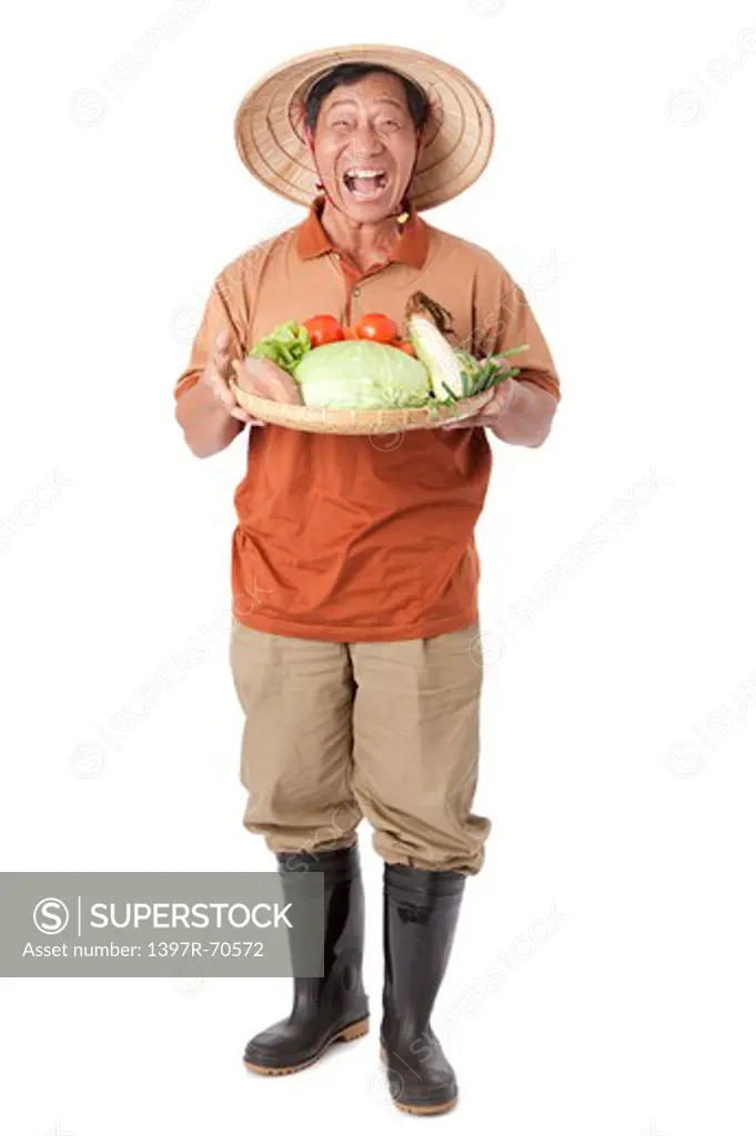 Elderly farmer standing and holding a sieve of vegetables, laughing